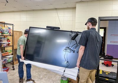 two men transporting a classroom distance learning monitor